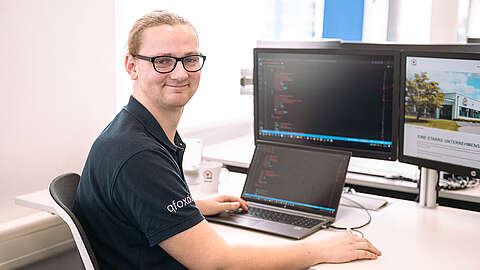 IT Service Desk als strategischer Erfolgsfaktor LEITDESK-Mitarbeiter sitzt an seinem Arbeitsplatz und lächelt in die Kamera