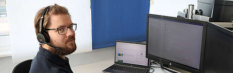 LEITDESK-Mitarbeiter sitzt mit Headset an seinem PC-Arbeitsplatz